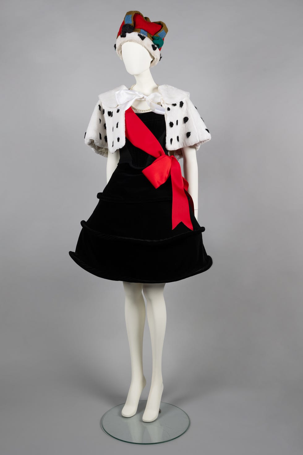 costume on a mannequin featuring a black dress with a red sash and a fur cape
