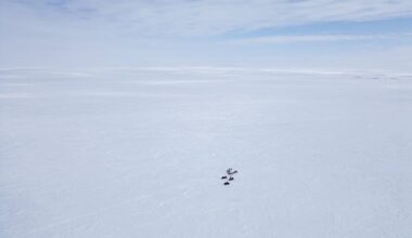 An aerial view of a handful of people dwarfed by a vast Arctic landscape dominated by sea ice.