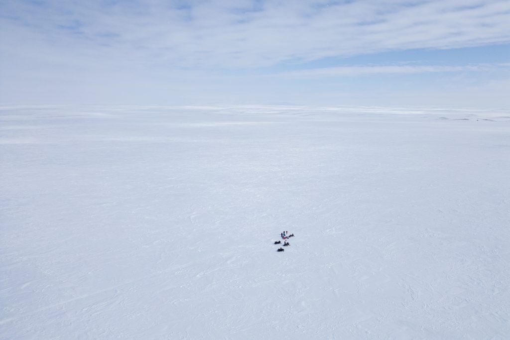 An aerial view of a handful of people dwarfed by a vast Arctic landscape dominated by sea ice.