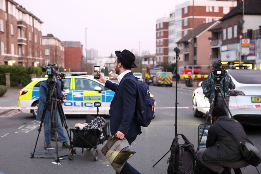 A man records using his mobile phone near the scene after four ambulances belonging to Hatzola, a Jewish community organisation, were set on fire in an incident that the police say is being treated as an antisemitic hate crime, in northwest London, on March 23, 2026.