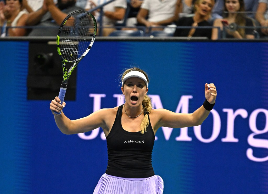 A female tennis player in a black top and light purple skirt, holding a tennis racket and celebrating a point with both arms raised.