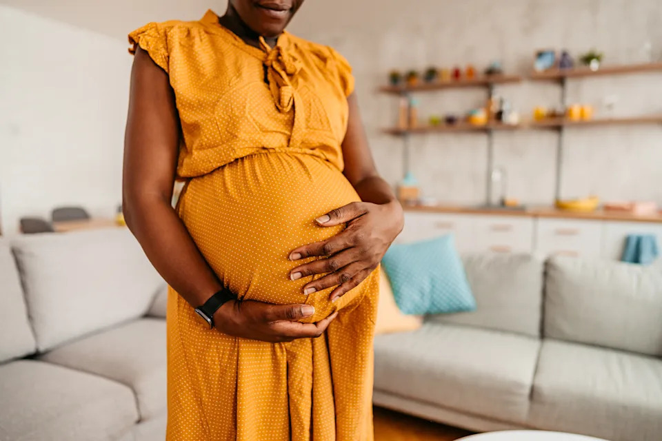 A person gently holding their pregnant belly in a relaxed living room setting