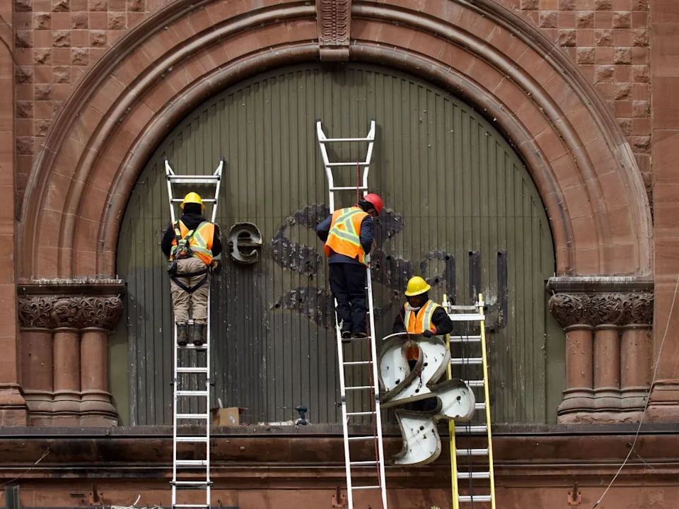  Workers on ladders help remove The Bay’s logo in downtown Montreal on Monday, March 9, 2026.