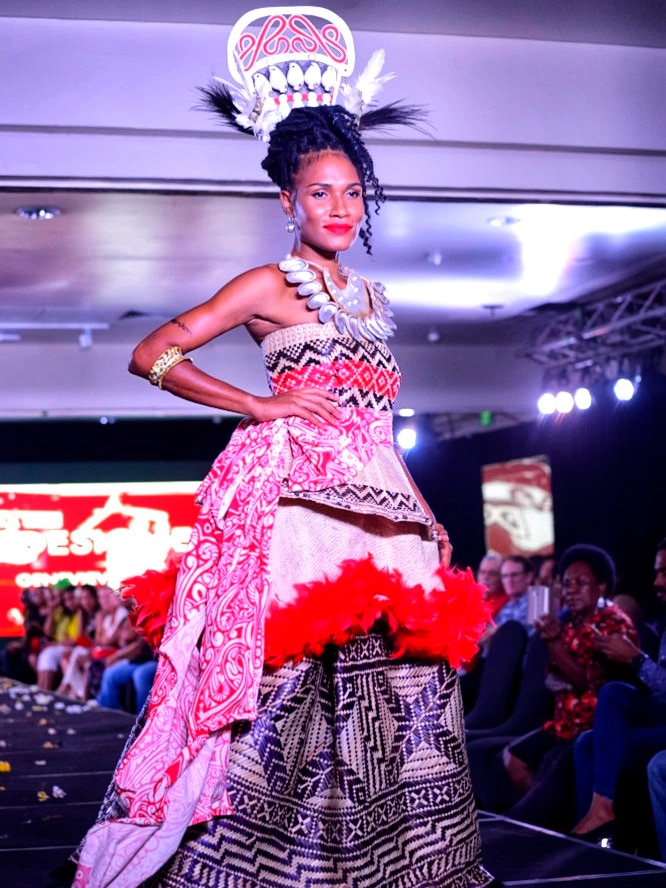 A young Papua New Guinean woman stands on a catwalk with hands on hips wearing traditional evening attire