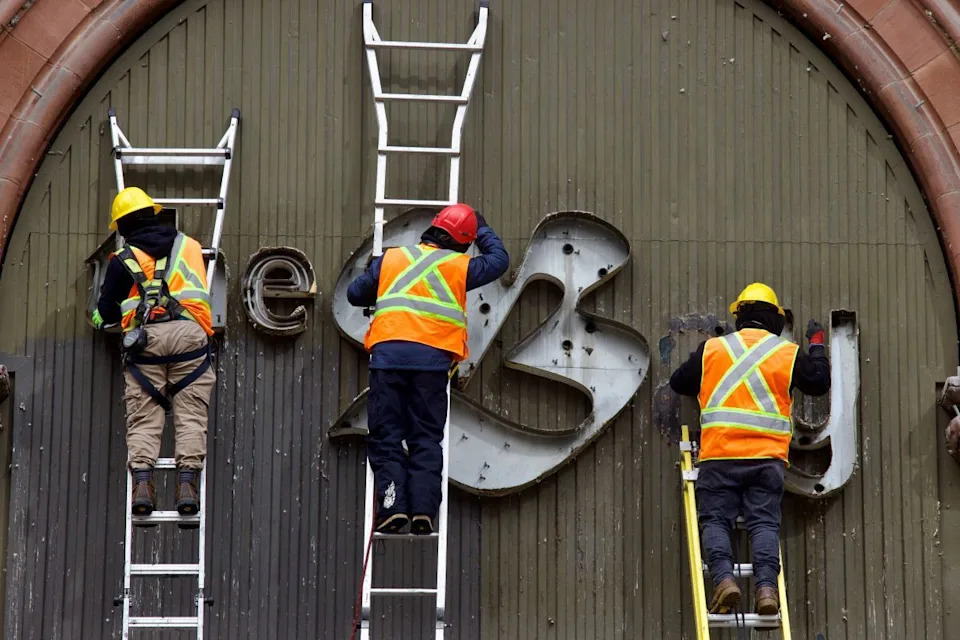  Workers take down the letters from The Bay sign at the old flagship store in downtown Montreal on Monday, March 9, 2026.