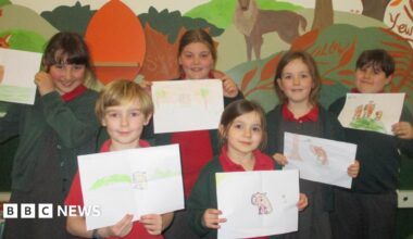 A group of schoolchildren wearing uniform hold up drawings of capybaras.