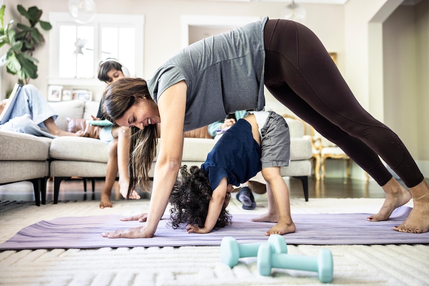 Mother exercising at home while distracted by toddler boy.