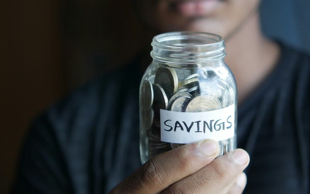 A young person holds a jar labelled savings.