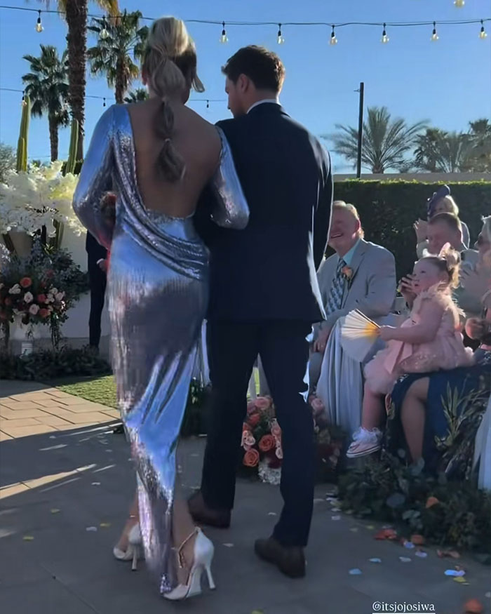 JoJo Siwa walking down the aisle with Chris Hughes at their wedding ceremony outdoors with guests watching.