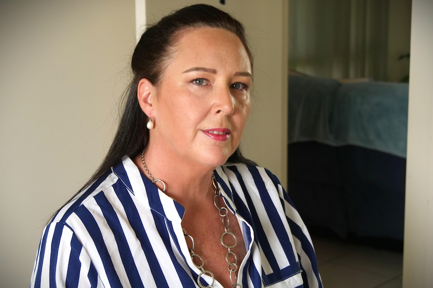 Joanna, a dark-haired woman standing wearing a blue-and-white striped shirt, silver, ringed necklace and red lipstick.