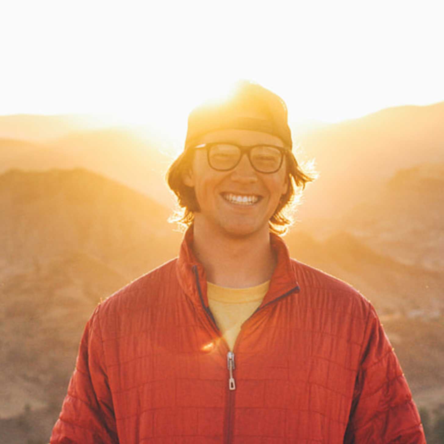 A young man smiles on a mountaintop as the sunsets.
