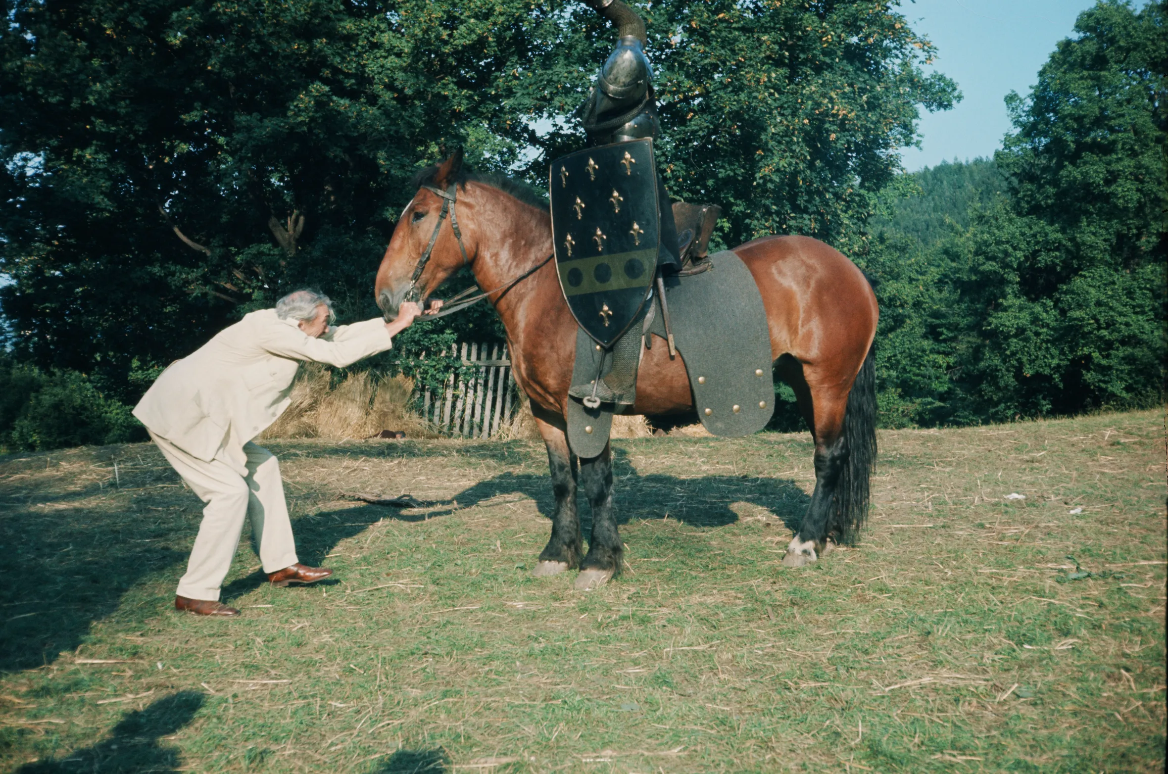 John Huston adjusting the bridle of a horse wearing knight's armor.