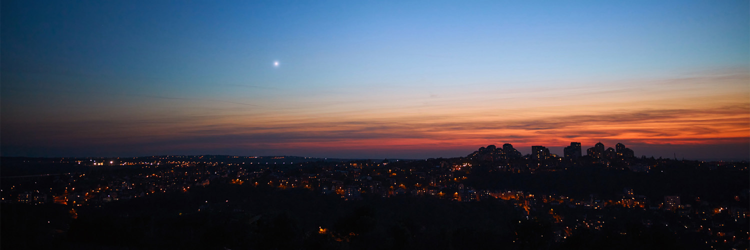 a bright star in the pre-dawn sky over a city