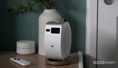 A BenQ GV32 projector rests on a wooden surface alongside its remote.