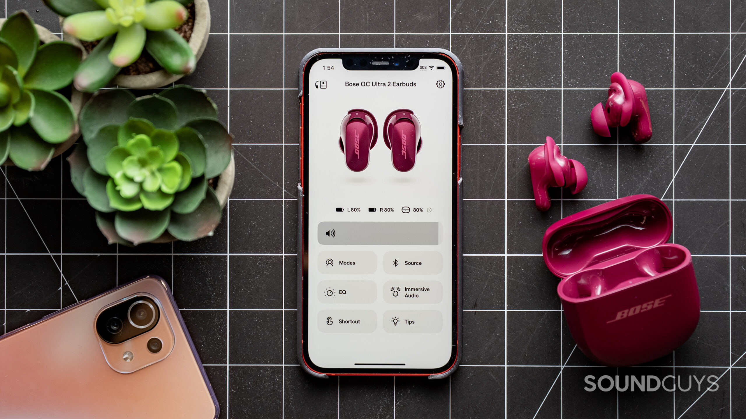 A photo of a phone with the Bose app open, showing the deep plum-colored Bose QuietComfort Ultra Earbuds on a table nearby.