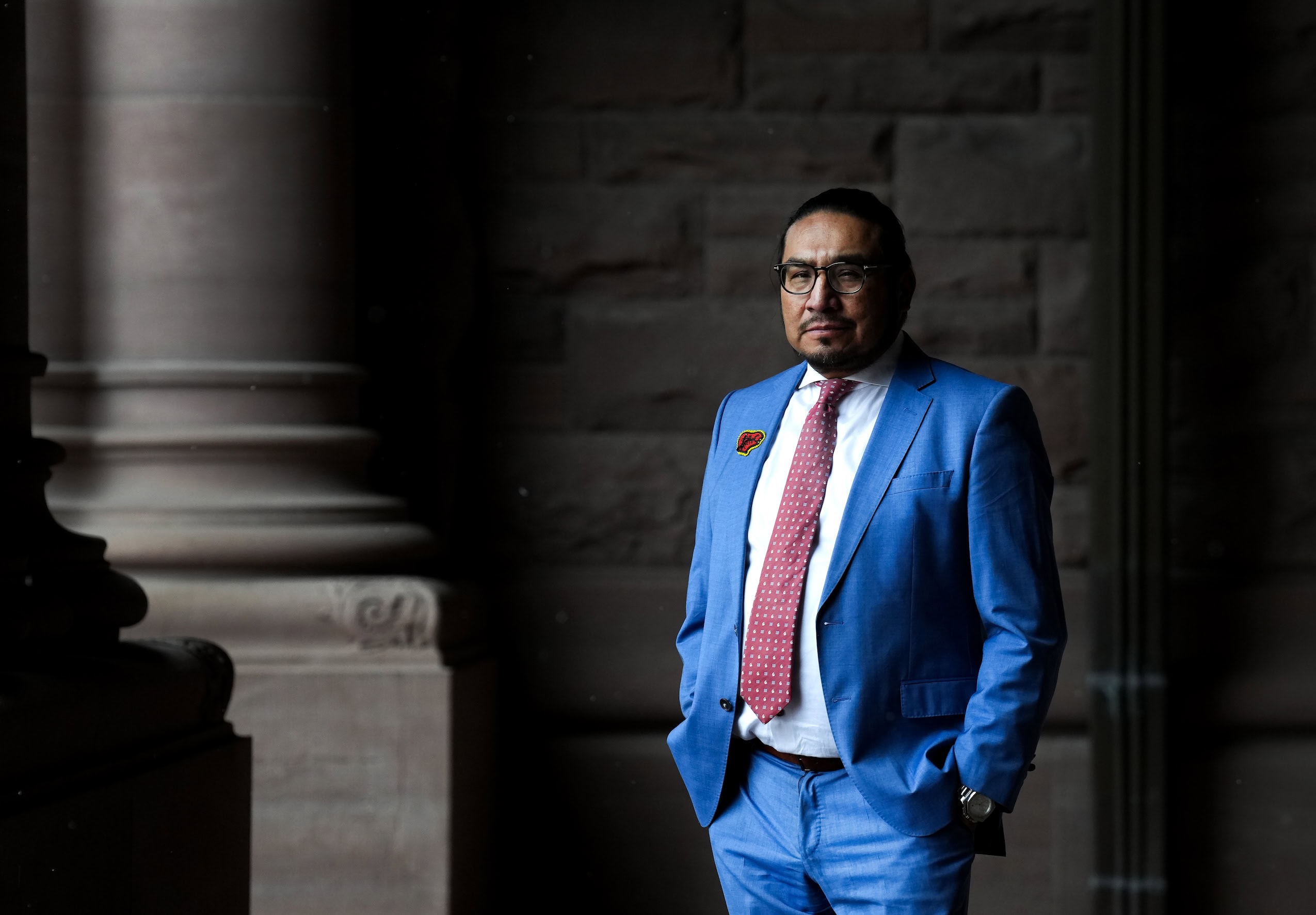 A portrait of MPP Sol Mamakwa taken at Queen's Park in Toronto on Nov. 27, 2025. Mamakwa is standing and wearing a blue suit with a red tie.