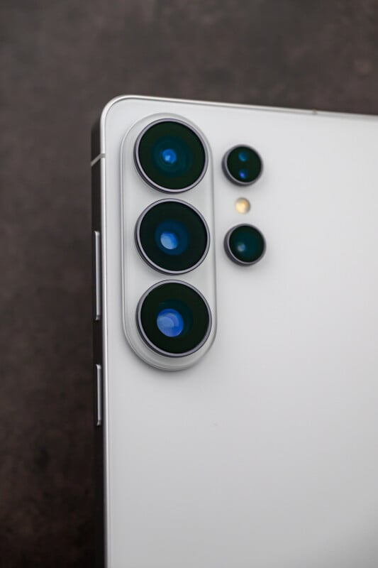 Close-up of the upper corner of a white smartphone showing three large rear camera lenses, a smaller sensor, and dual LED flash against a dark background.