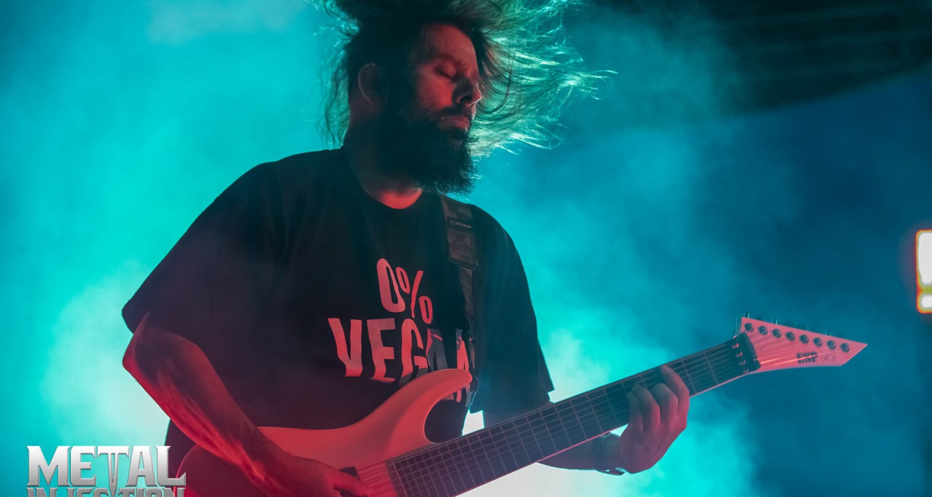 Stephen Carpenter playing guitar on stage during a live Deftones concert, with dramatic stage lighting and audience in the background.