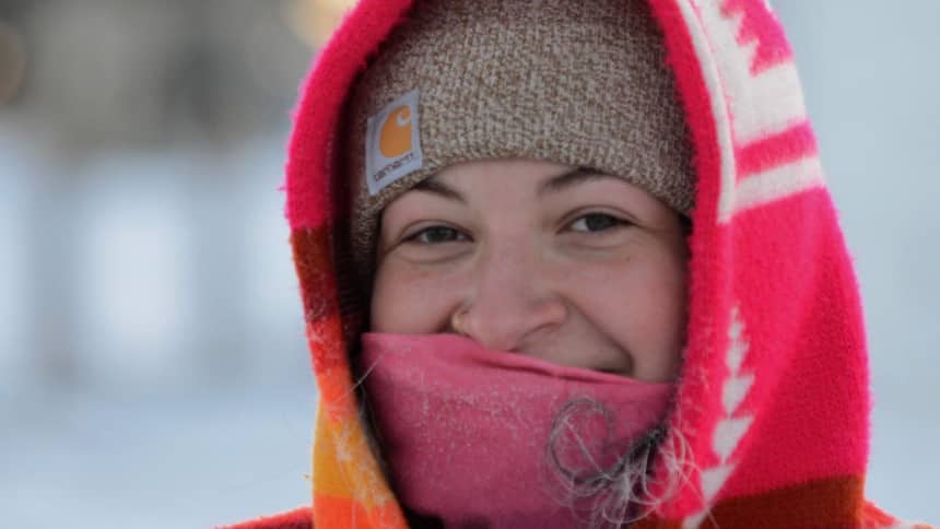 A girl smiling beneath a neck scarf, toque and bright coloured hood.