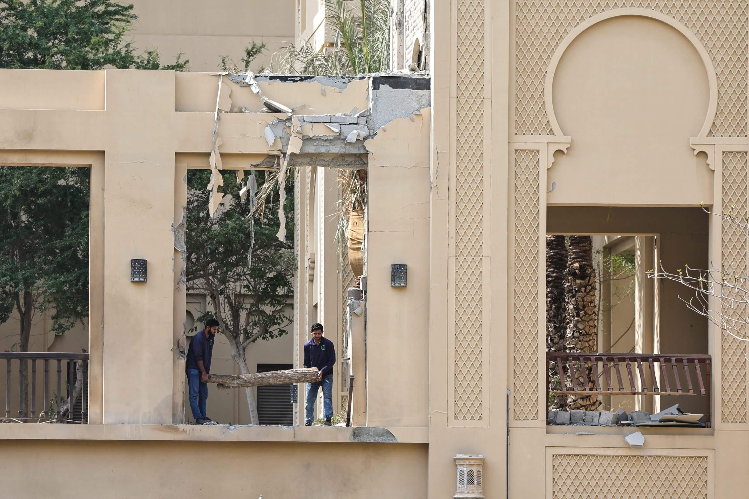 Workers clear debris from a white stone palatial building with visible damage on its front.