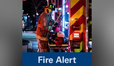Firefighter beside a fire truck with emergency lights on at night.
