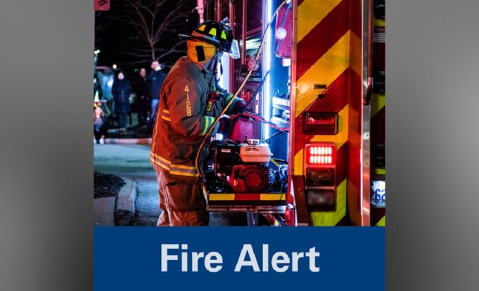 Firefighter beside a fire truck with emergency lights on at night.
