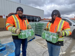 Two men in orange vests hold cases of water