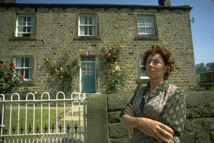 Sheila Mercier Annie Sugden, arms crossed, stood outside of the original Emmerdale Farmhouse in 1972
