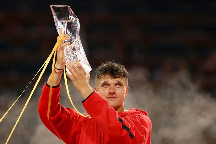 Tennis player Jakub Mensik, in a red sports jacket, holds up the Miami Open trophy.