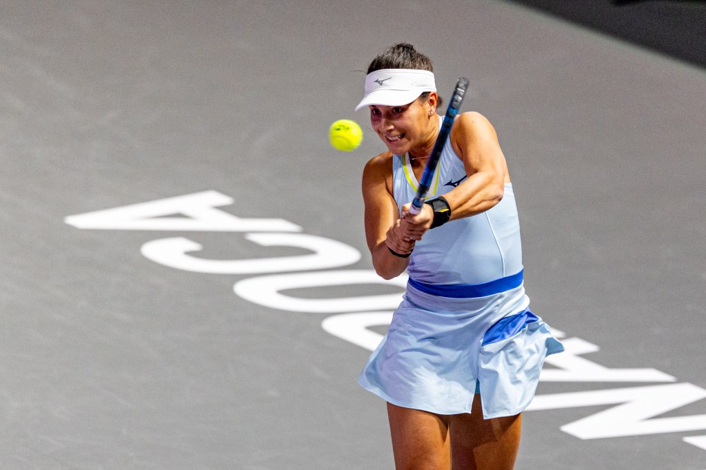 A female tennis player in a light blue outfit and visor hits a tennis ball with a racket.