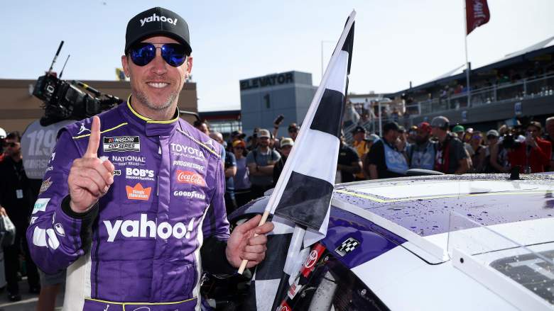 Denny Hamlin celebrates a NASCAR Cup Series win while holding the checkered flag beside his No. 11 Joe Gibbs Racing Toyota.