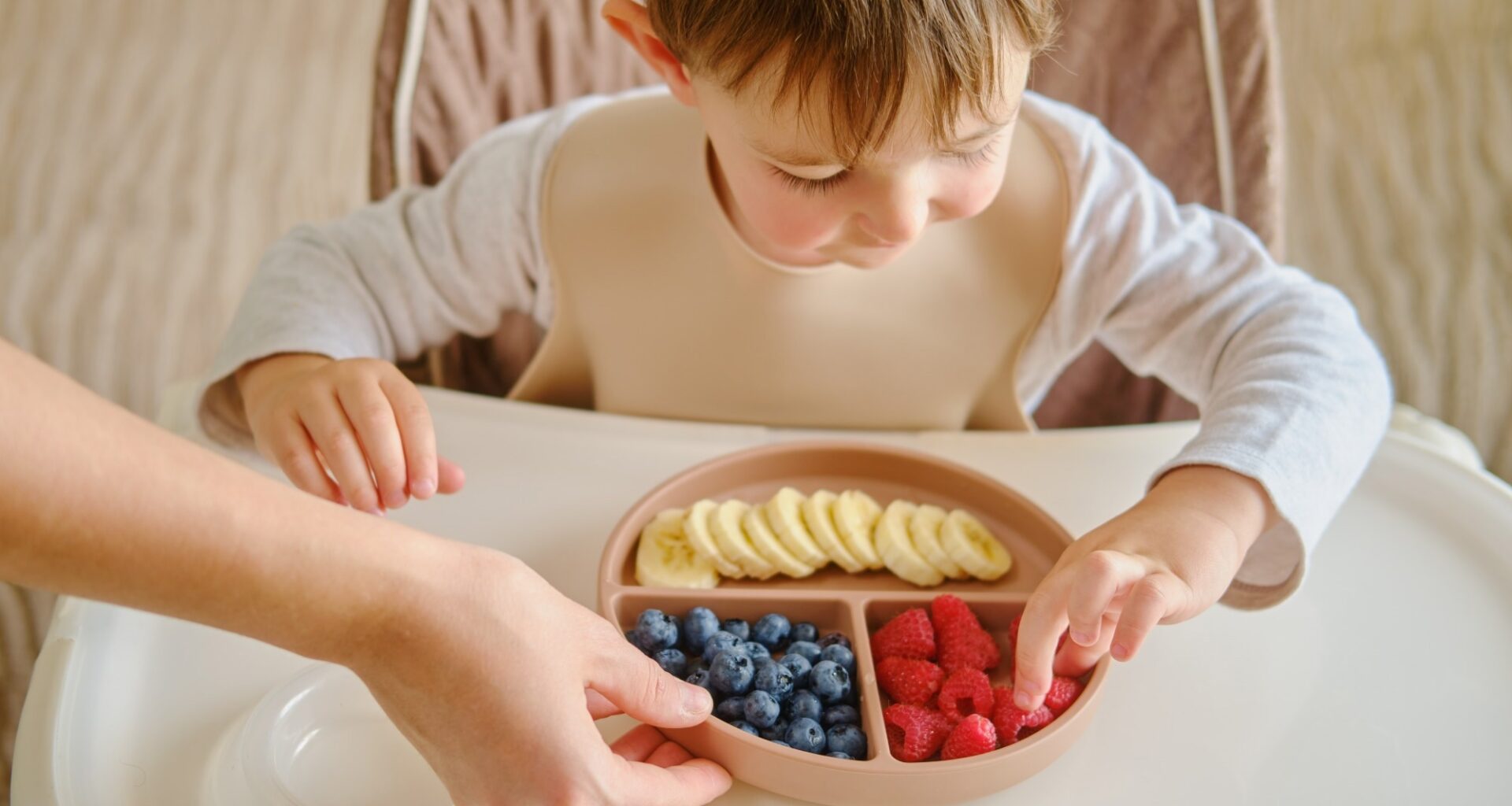 A mother woman gives her child a plate of fruits and berries
