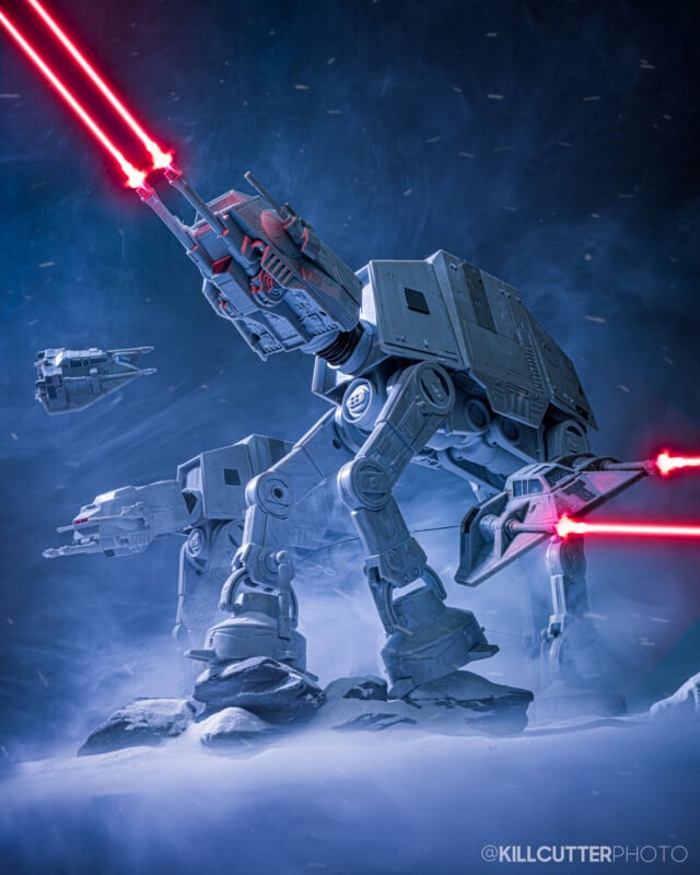 Two Star Wars AT-AT walkers fire bright red lasers in a snowy, foggy environment. A smaller vehicle flies nearby. The scene is dramatic with a dark blue background and dynamic lighting.