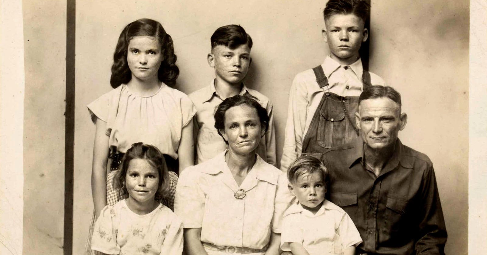 A black-and-white portrait of a family from the early 20th century, showing two adults and four children. The adults are seated in front, with the children standing and sitting around them, all facing the camera with neutral expressions.