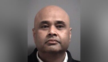 headshot photo of a middle-aged man facing the camera. He has a shaved head, a slight moustache and stubble, and is wearing a dark jacket.