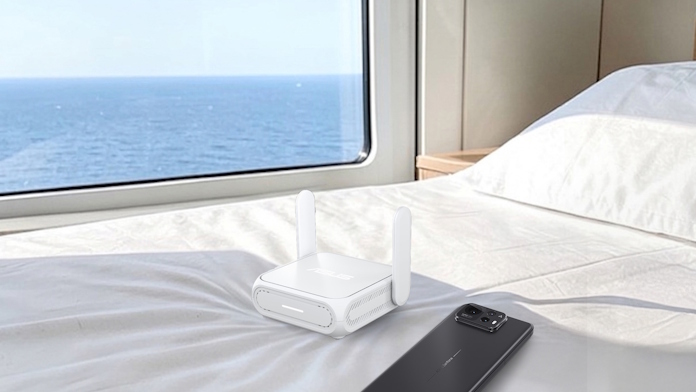 An ASUS travel router on a bed near an open window with an ocean view