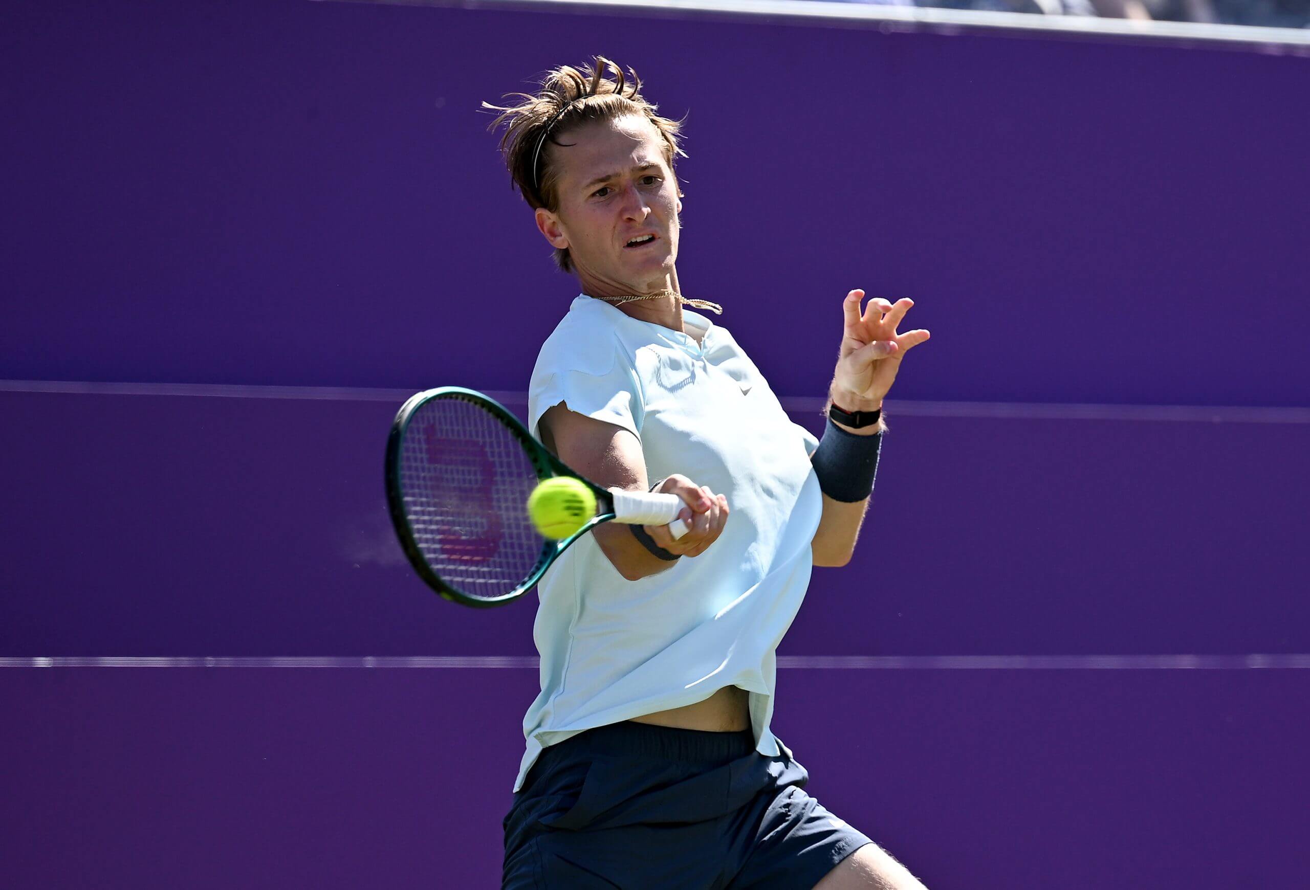 Sebastian Korda hits a forehand with his eyes on the ball against a purple background