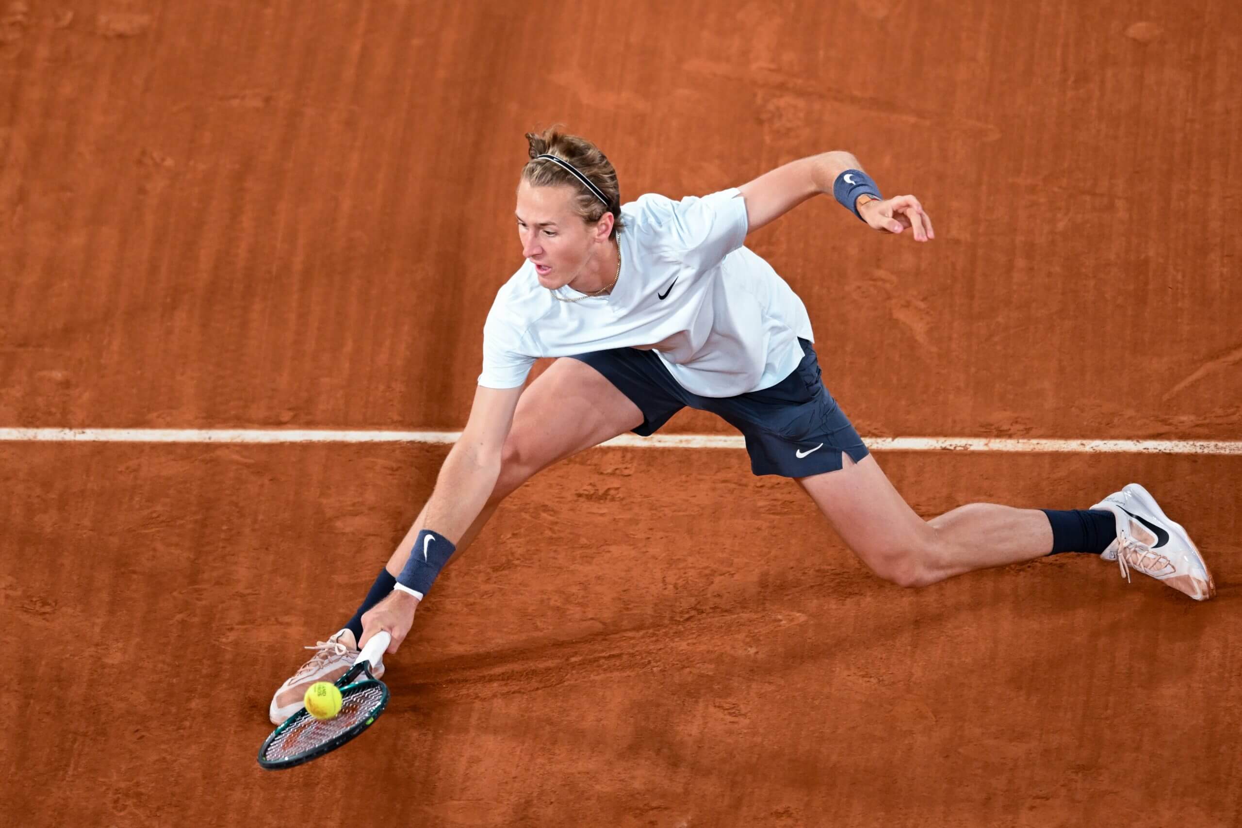 Sebastian Korda meets a low backhand volley stretching forward on a clay court.