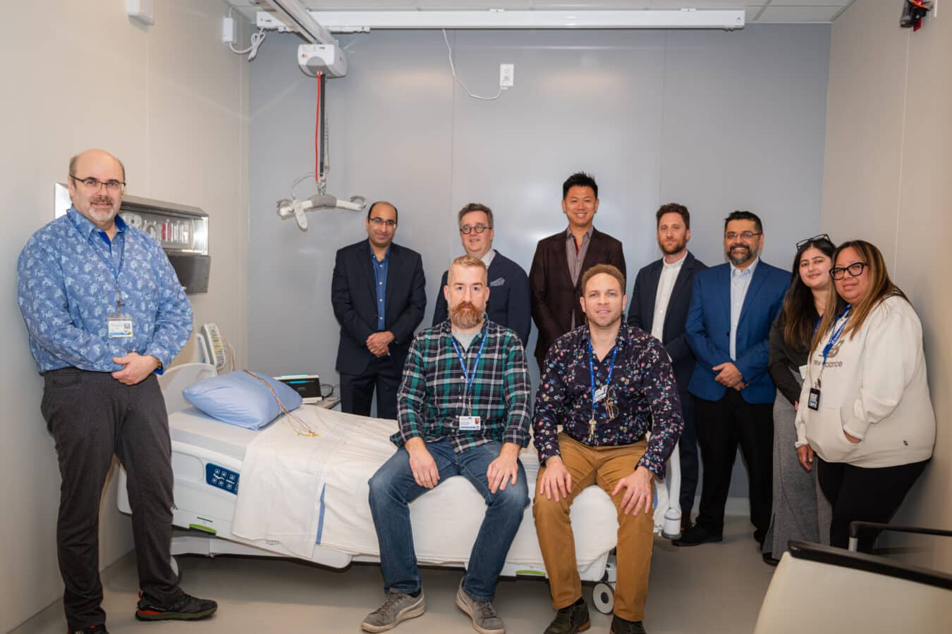 Ten healthcare staff members pose together in a hospital sleep laboratory beside a patient bed with sleep study monitoring equipment.