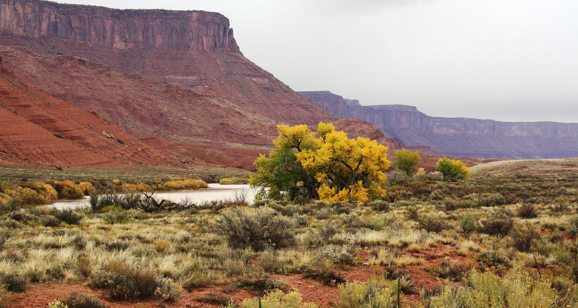 A larger reddish butte overlooks a flowing river with sage and brush on either side