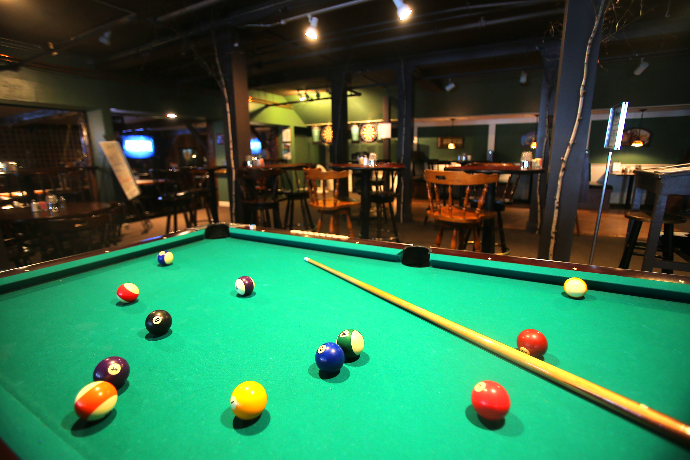A green pool table with multiple balls and a cue