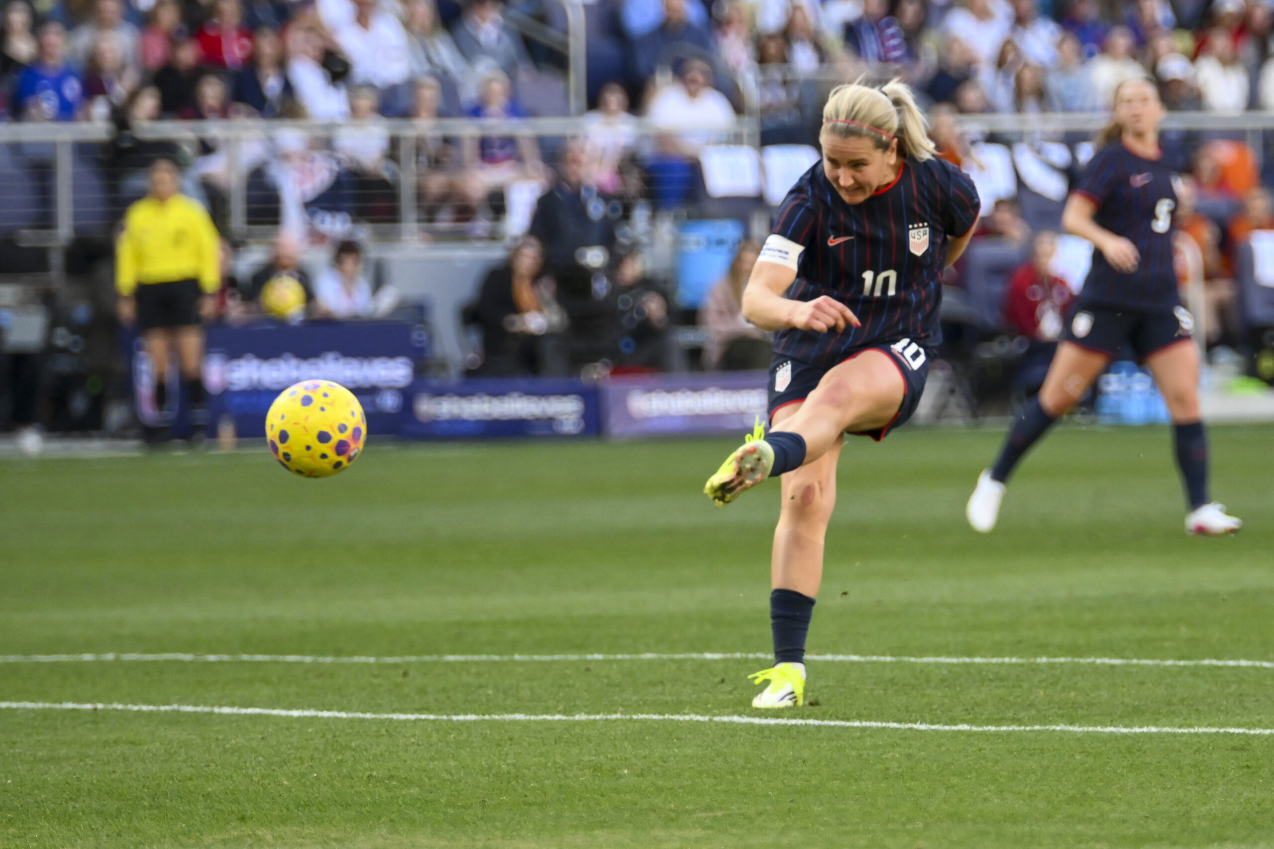 A player wearing a blue uniform kicks the ball on a soccer field