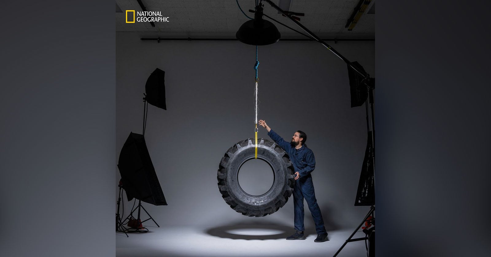 A man in a studio setting stands next to a large tire hanging from the ceiling by a rope. He is touching the tire, and professional lighting equipment is visible around him. The National Geographic logo appears in the top left corner.