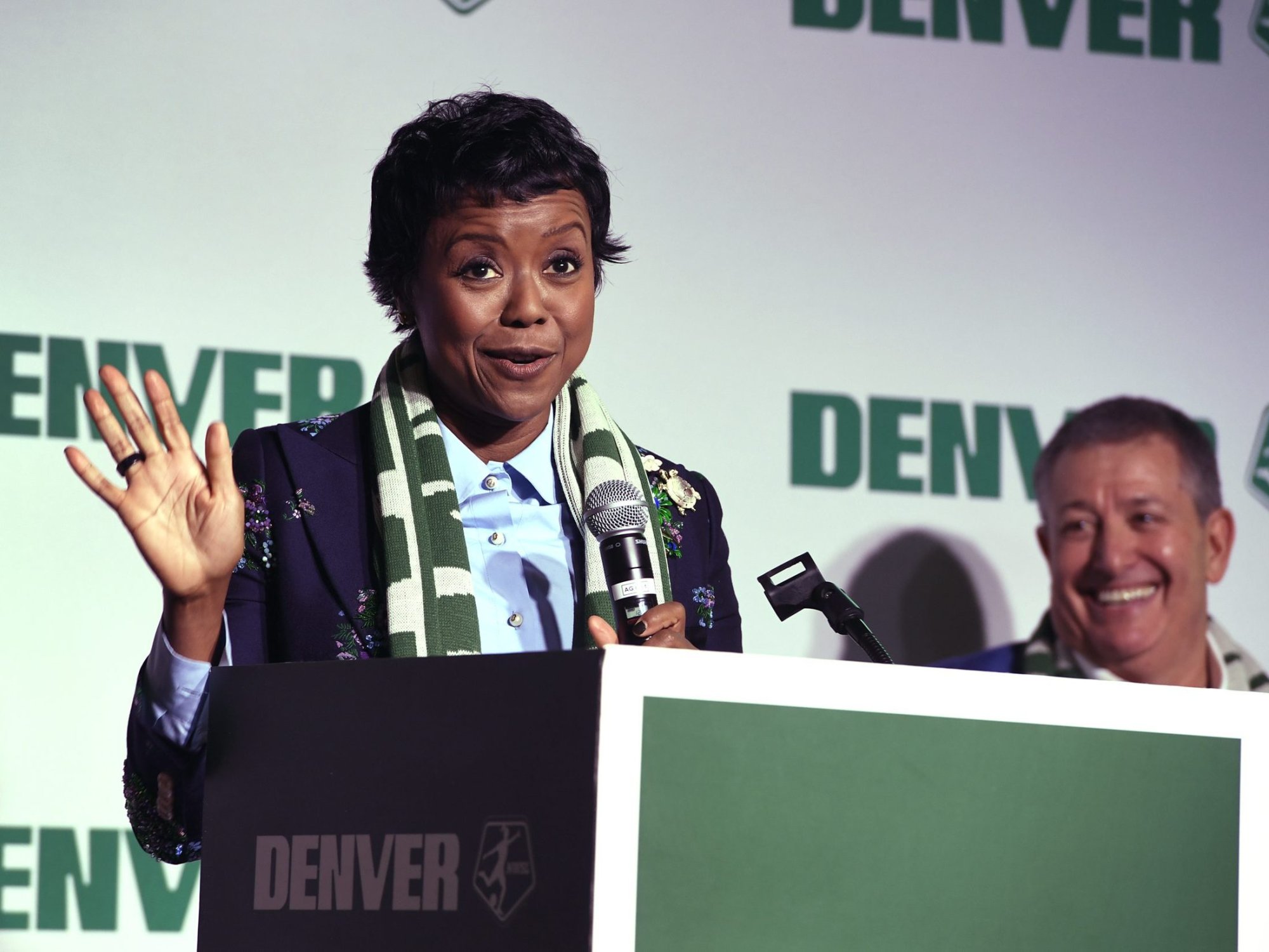 Mellody Hobson, who is wearing a flowered blazer and a green and white scarf gestures with her hand as she talks about Denver's new women's professional soccer team.