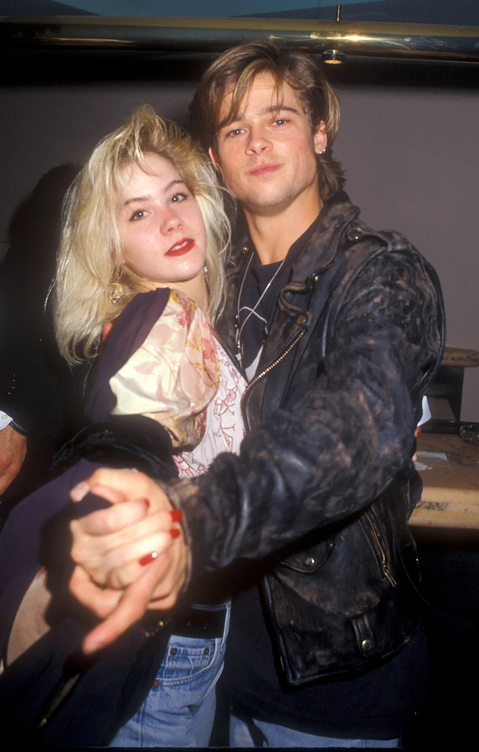 Applegate and Brad Pitt pose together at an event, with him in a dark leather jacket and her with platinum blonde hair