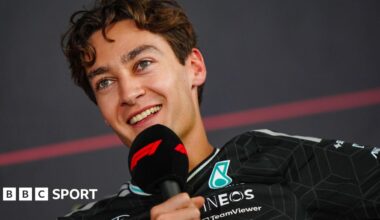 A smiling George Russell speaking into an F1-branded microphone during a news conference at Bahrain testing