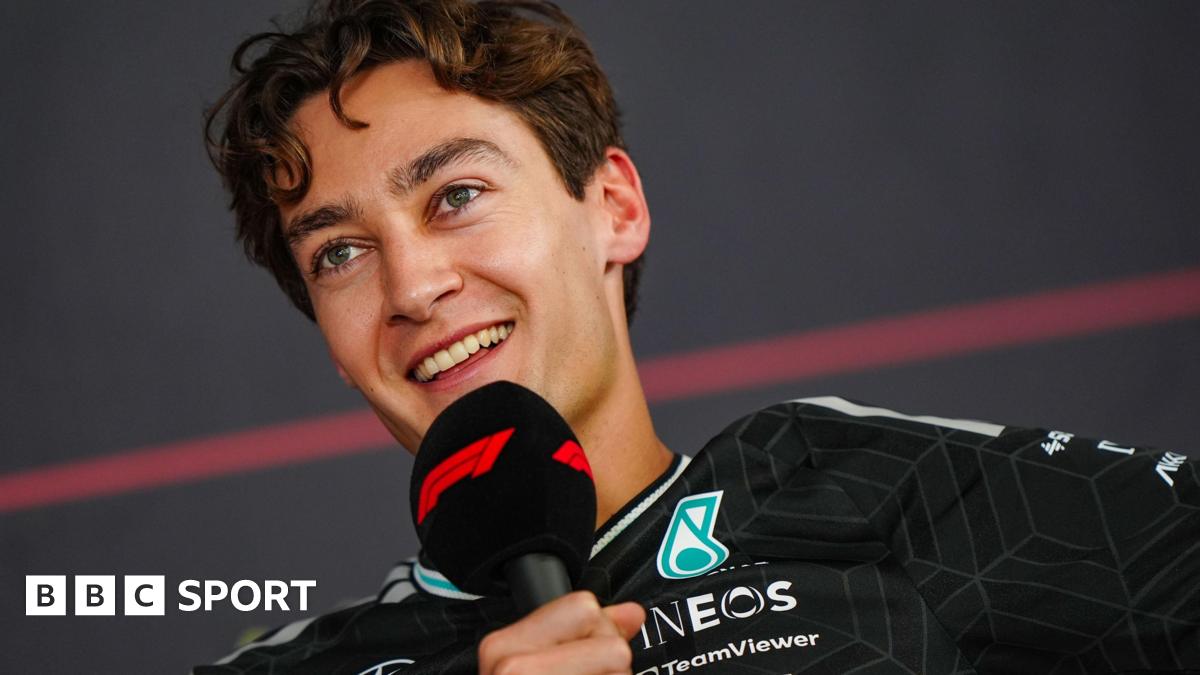 A smiling George Russell speaking into an F1-branded microphone during a news conference at Bahrain testing