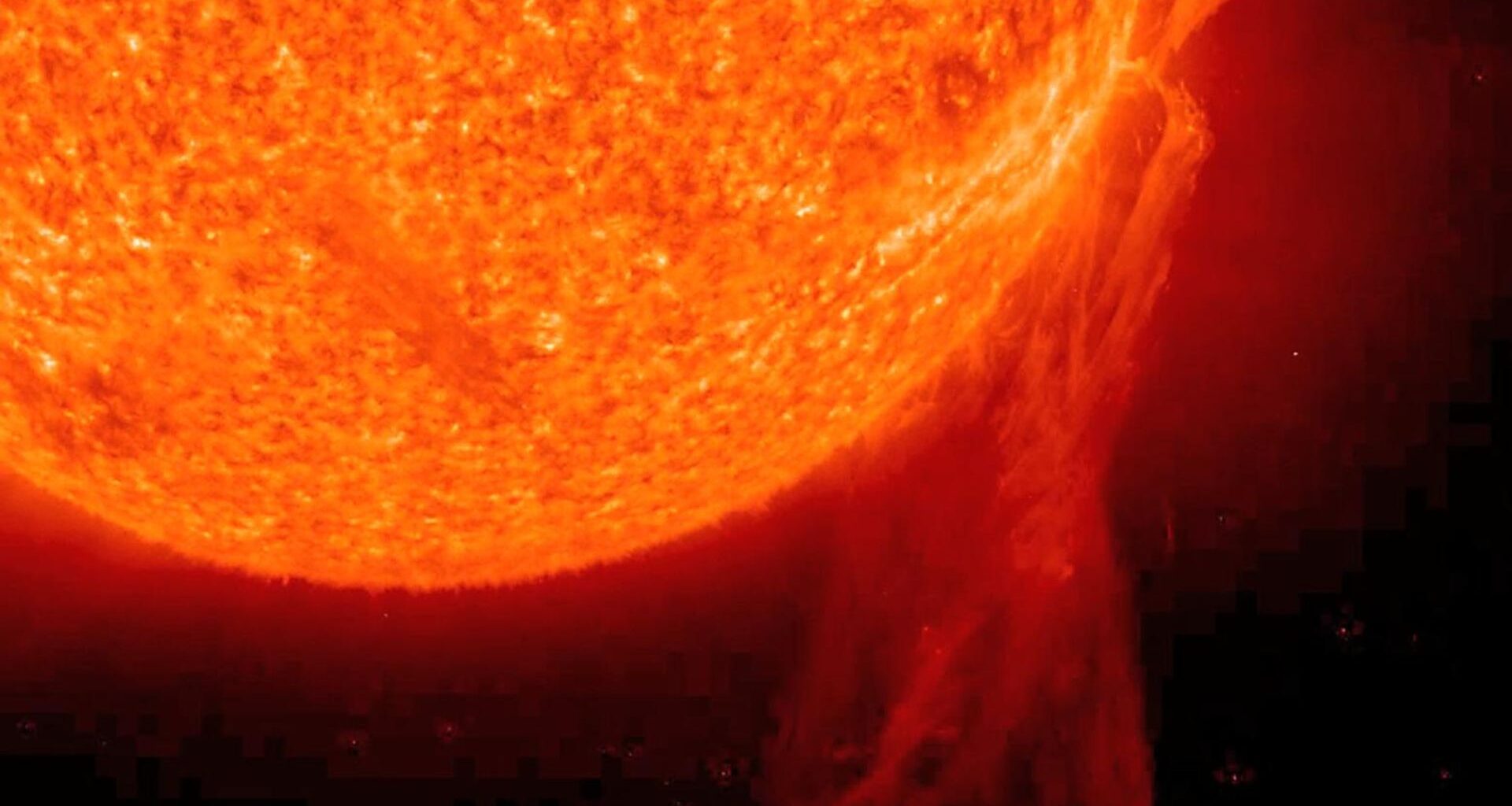 A close up of the sun shows a glowing orange and red ball of gas with long streaks of gas filaments leaking from its surface into the darkness of space.