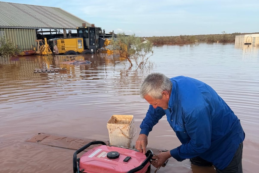 A man tries to start a generator in a flooded field.