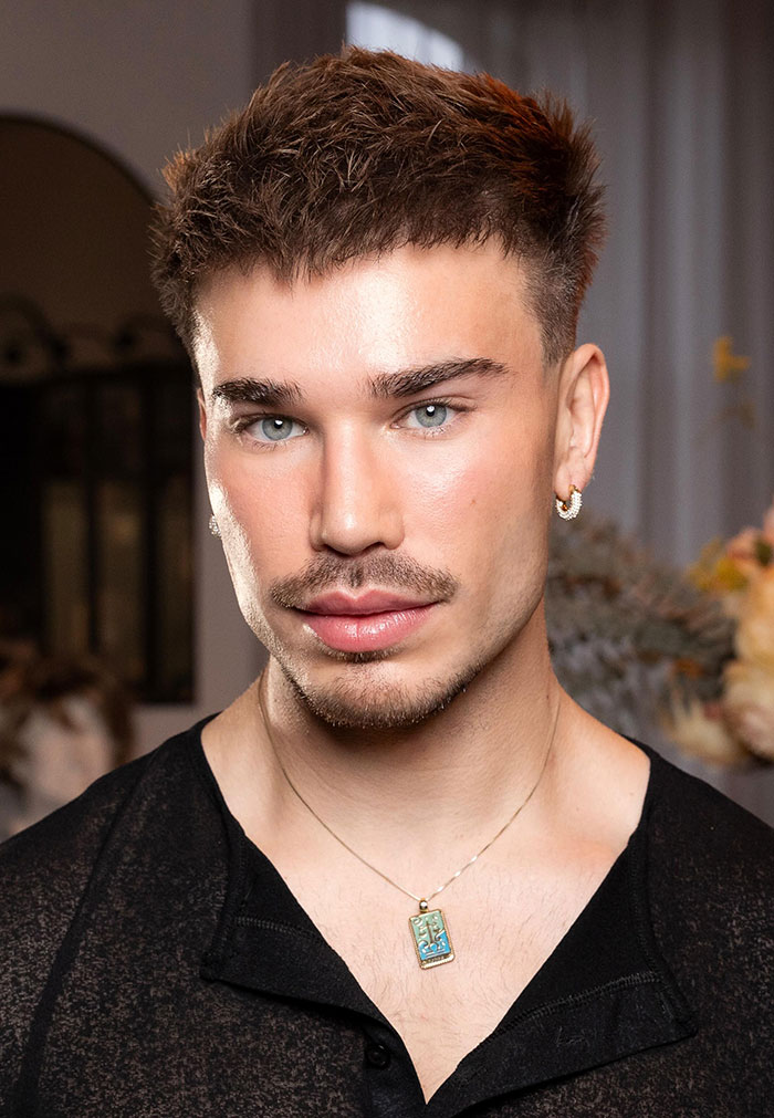 Young man with styled hair and earrings posing indoors, related to Jim Carrey theories and drag queen mask reveal. Young man with styled hair and earrings posing indoors, related to Jim Carrey theories and drag queen mask reveal.